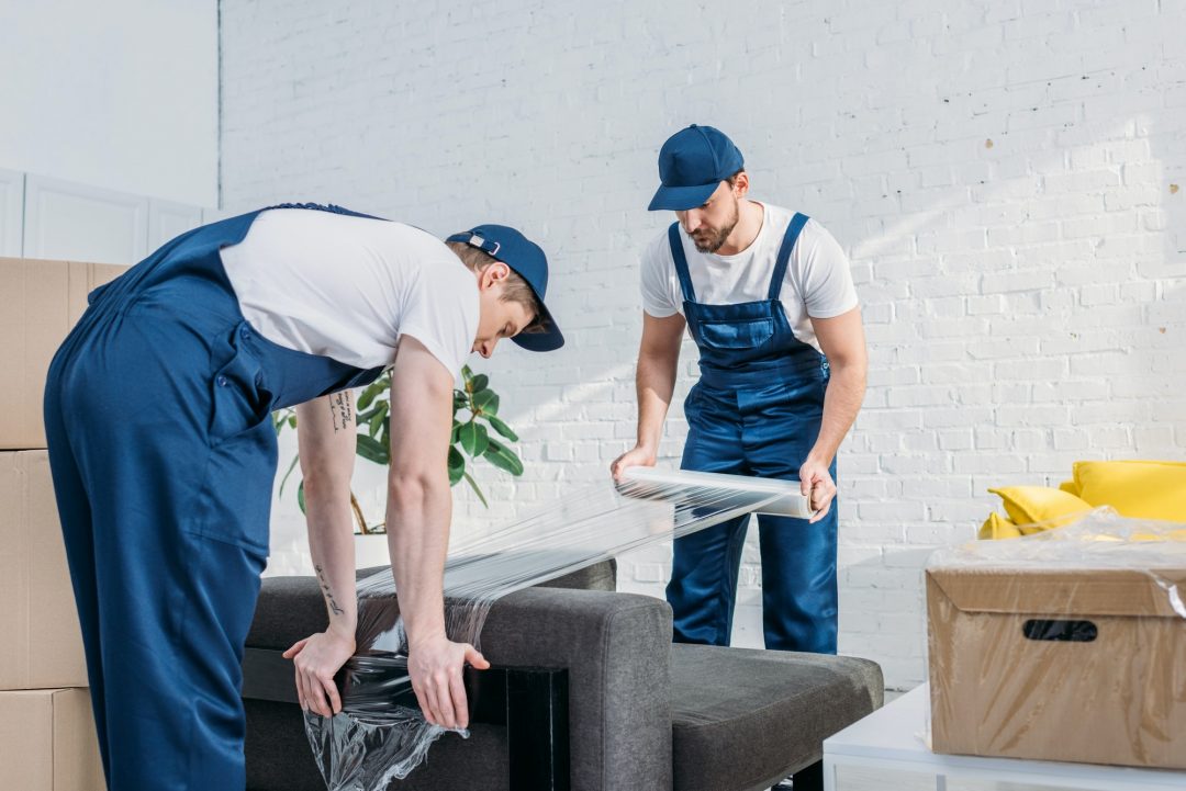 Umzugshelfer wickeln Sofa mit Stretchfolie in Wohnung ein